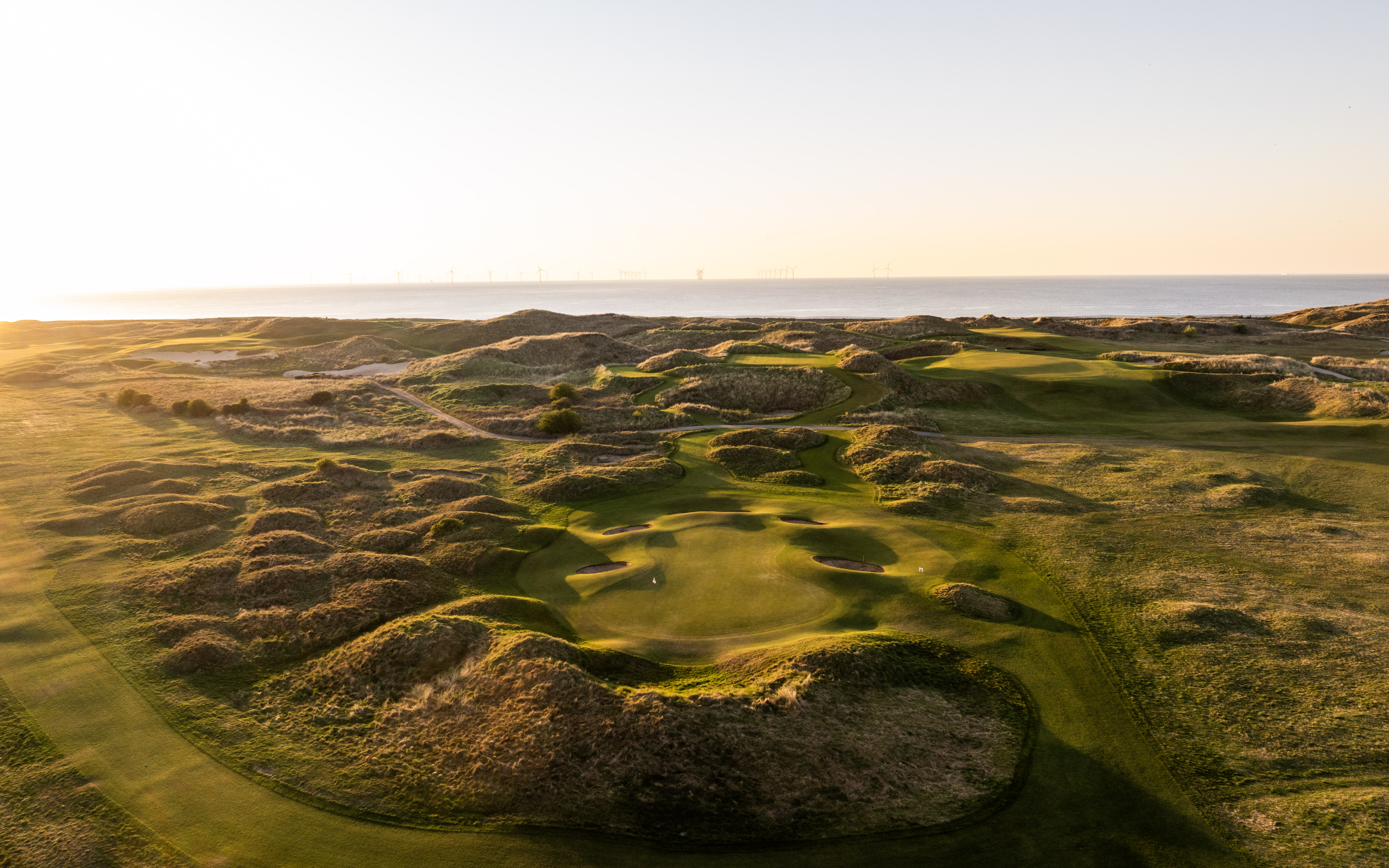 A green cupped in the dunes from the air, bunkers either side and the sea beyond